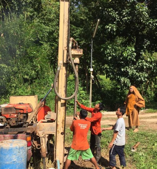 Group of men working equipment to dig a water well in a field