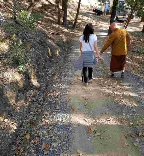 Monk and woman walking down a dirt road inspecting the sides covered with gravel