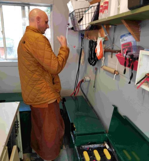 Monk standing in front of several boxes of large batteries on the floor of a shed