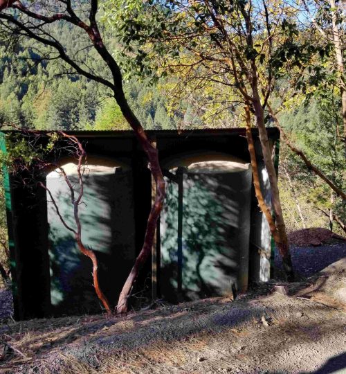 Two large water tanks on a mountain with trees in the background