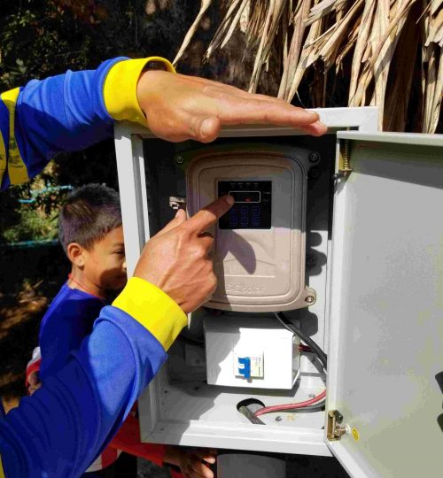 Man pointing to DC electrical equipment with boy in the background